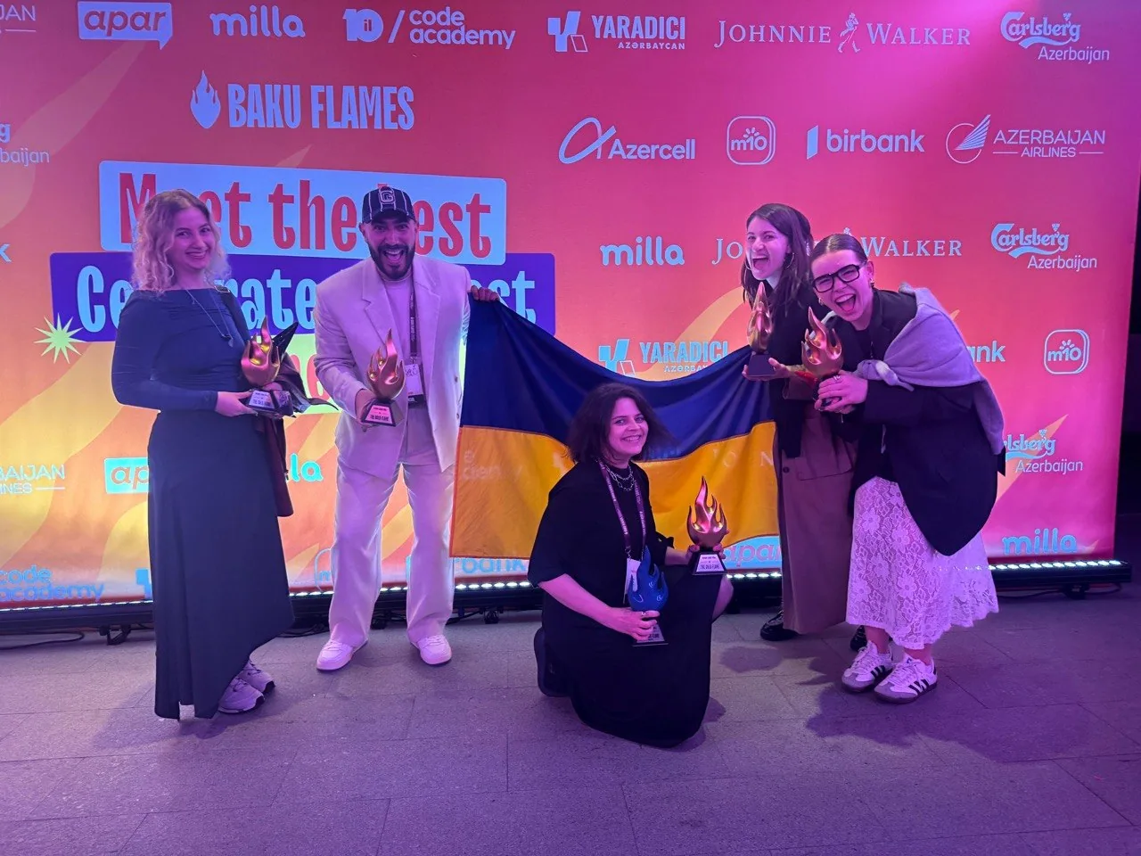 The team on stage with trophies and a Ukrainian flag
